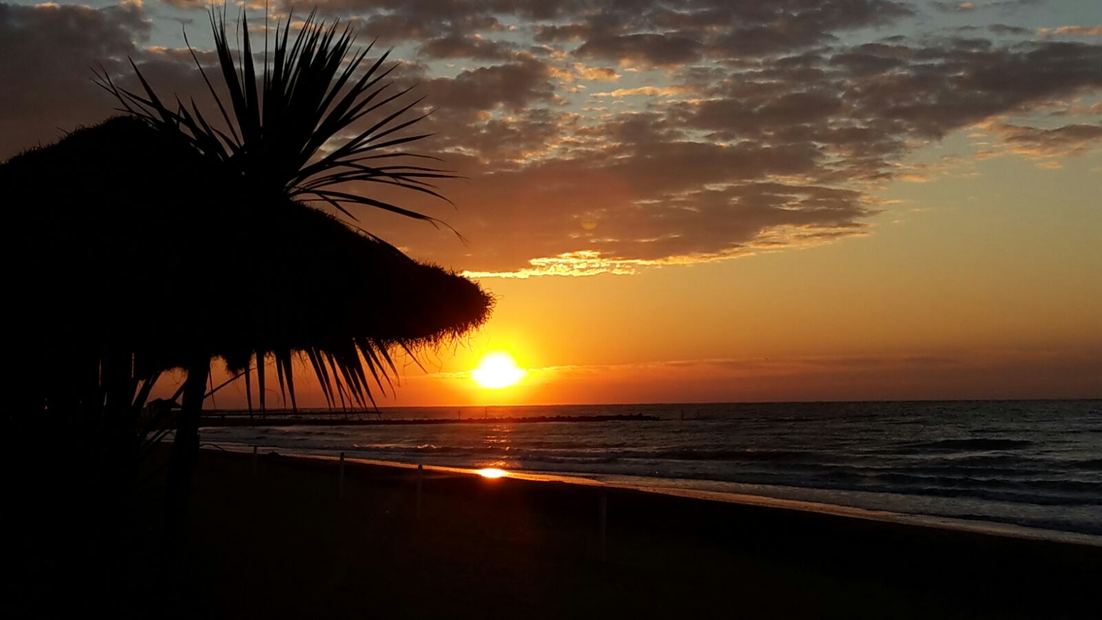Tramonto sul mare visto da sotto un ombrellone di paglia